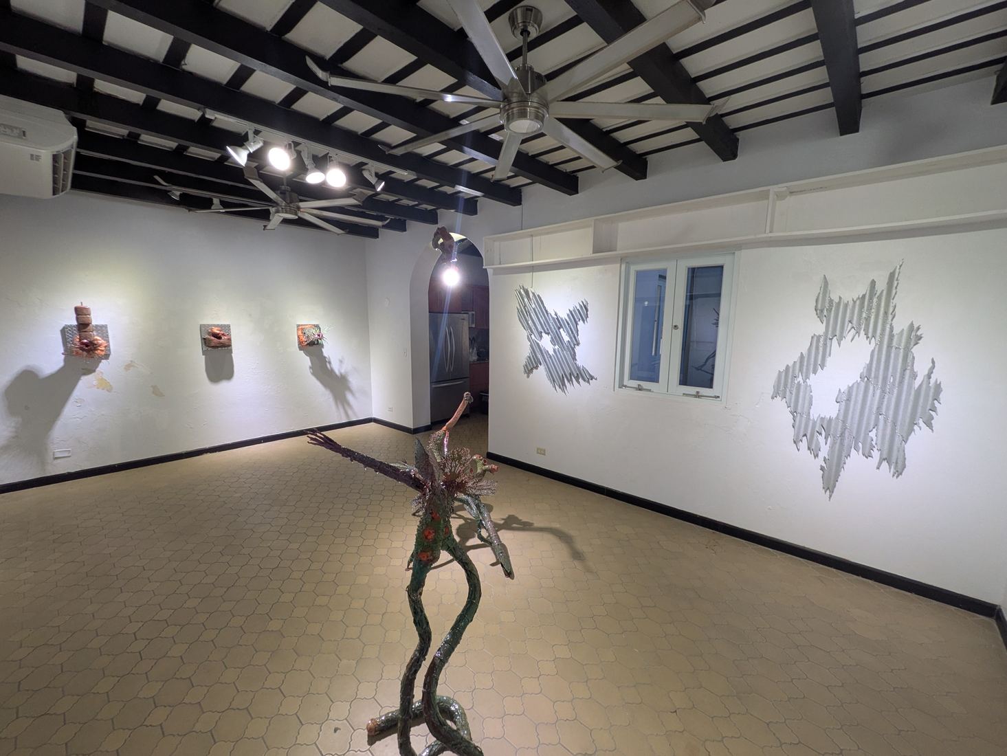 Gallery room with sculptural wall works and a standing sculpture