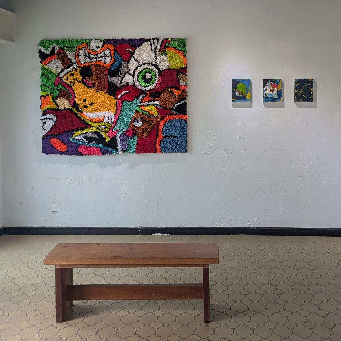 Large textile work beside three small paintings
